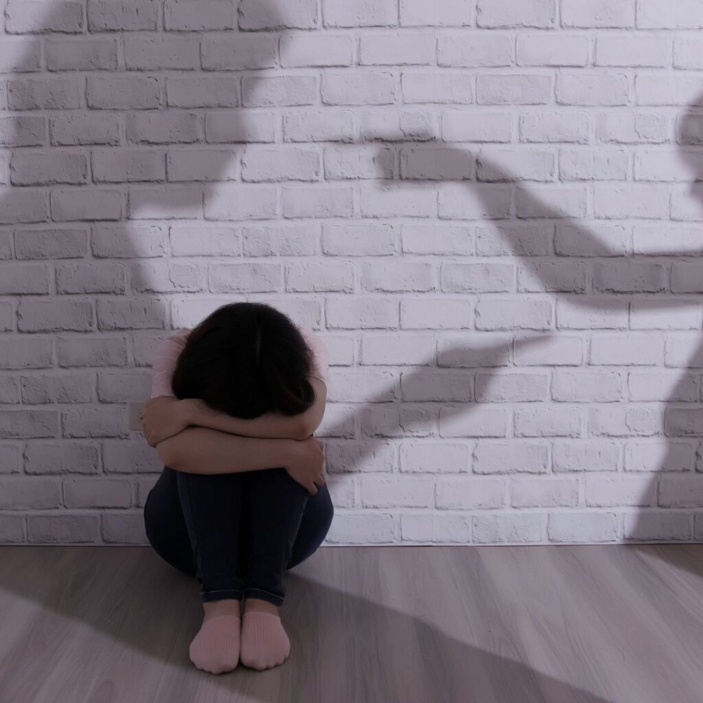 person hugging knees in shadow of people fighting